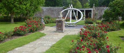 Sundial feature in walled garden with red roses