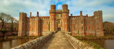 View of a red brick castle across drawbridge over moat